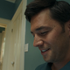 A man smiles downwards at something off-camera.